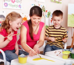 Kindergärtnerin malt mit Kindern ein Bild